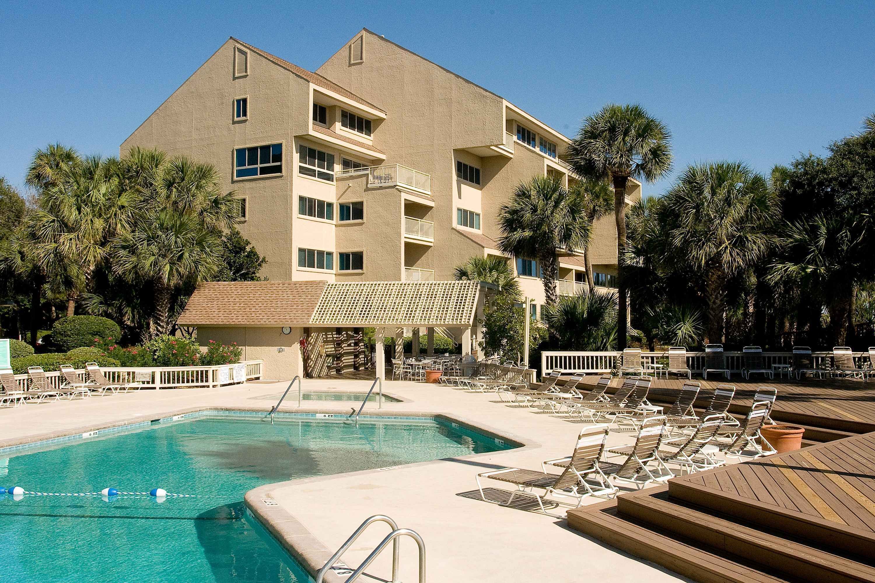 A hotel with a swimming pool, lounge chairs, and palm trees.