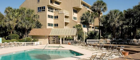 A hotel with a swimming pool, lounge chairs, and palm trees.