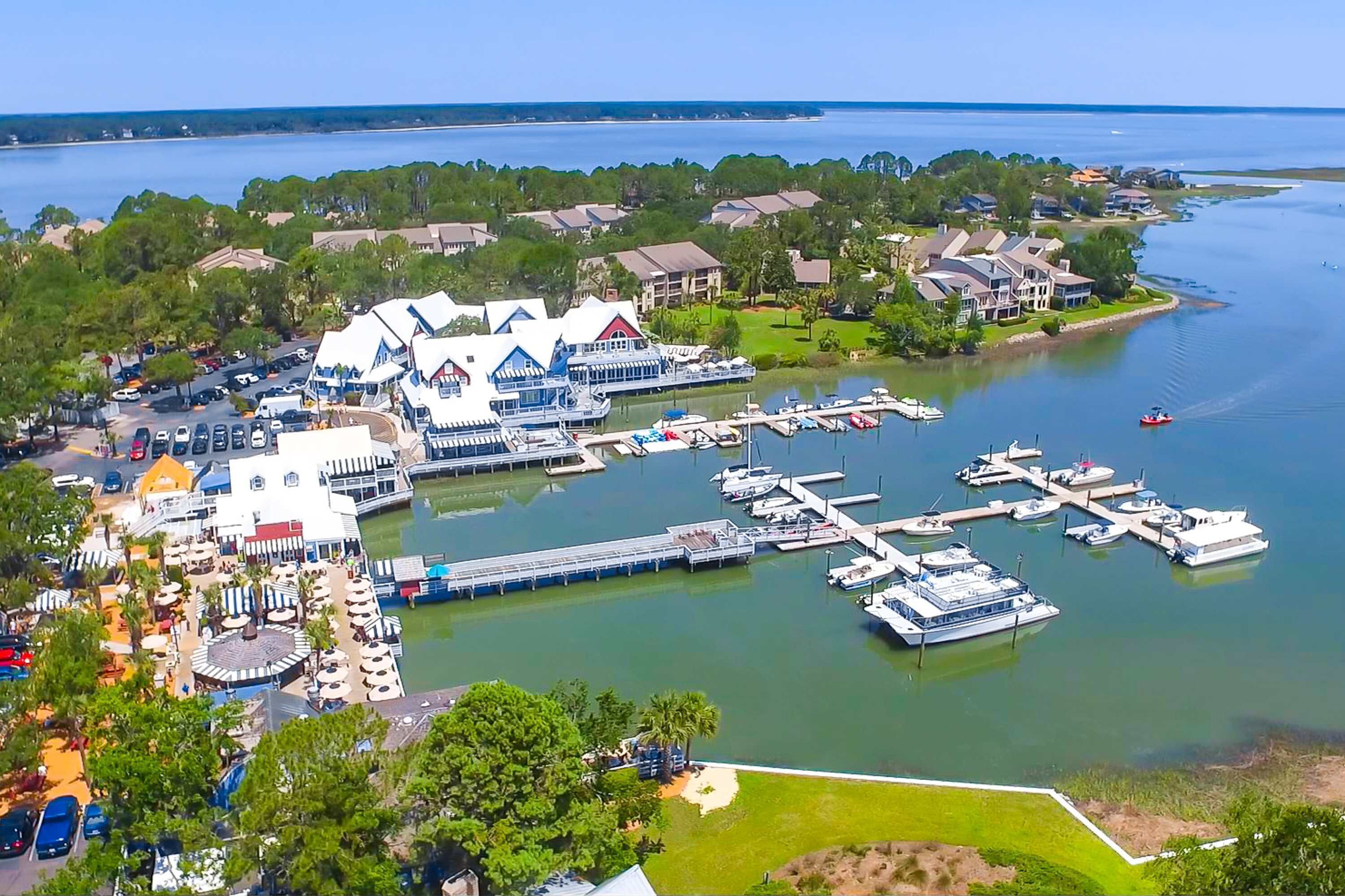 An aerial view of a marina with boats docked, a large building with a white facade, and surrounding residential areas.