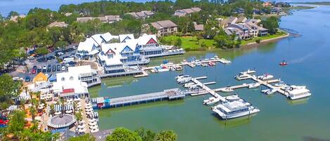 An aerial view of a marina with boats docked, a large building with a white facade, and surrounding residential areas.
