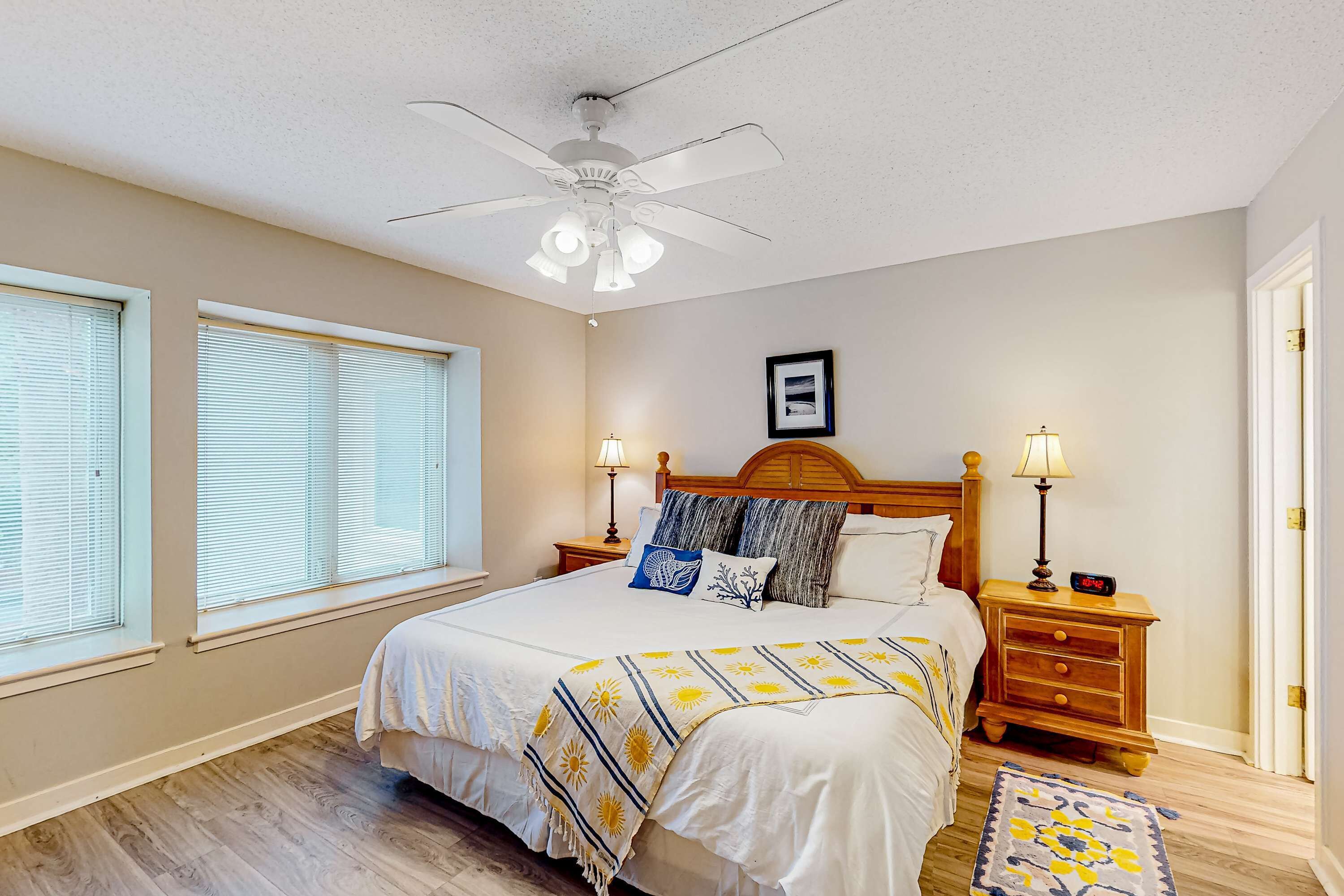 A bedroom with a bed, two bedside tables, a ceiling fan, and a window with blinds.