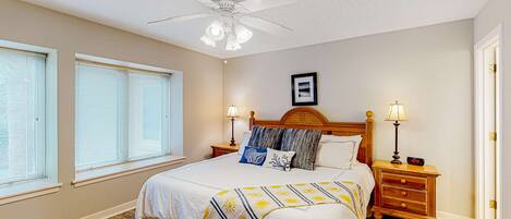 A bedroom with a bed, two bedside tables, a ceiling fan, and a window with blinds.