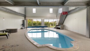 Une piscine intérieure offrant une vue dégagée sur l’extérieur, un espace couvert avec des sièges et un poste de surveillance pour les sauveteurs.