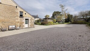 Un bâtiment en pierre avec une allée gravillonnée, un banc et un petit espace aménagé en jardin.