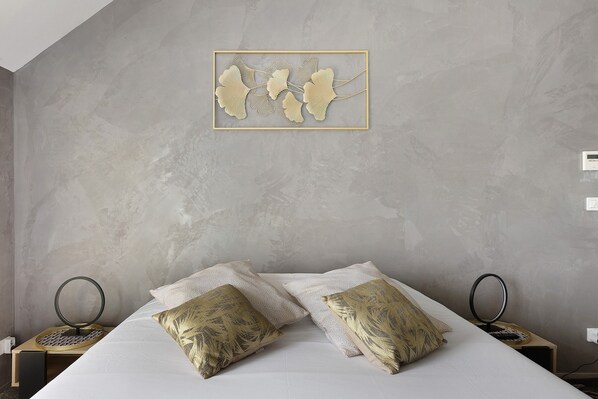 Une chambre à coucher comprenant un lit, deux tables de chevet, une lampe fixée au mur et une œuvre d’art encadrée.
