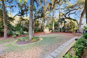 A well-maintained garden with a stone pathway, surrounded by tall trees and various shrubs. - Beautifully renovated Sea Pines home with private hot tub & large outdoor space (Hilton Head)