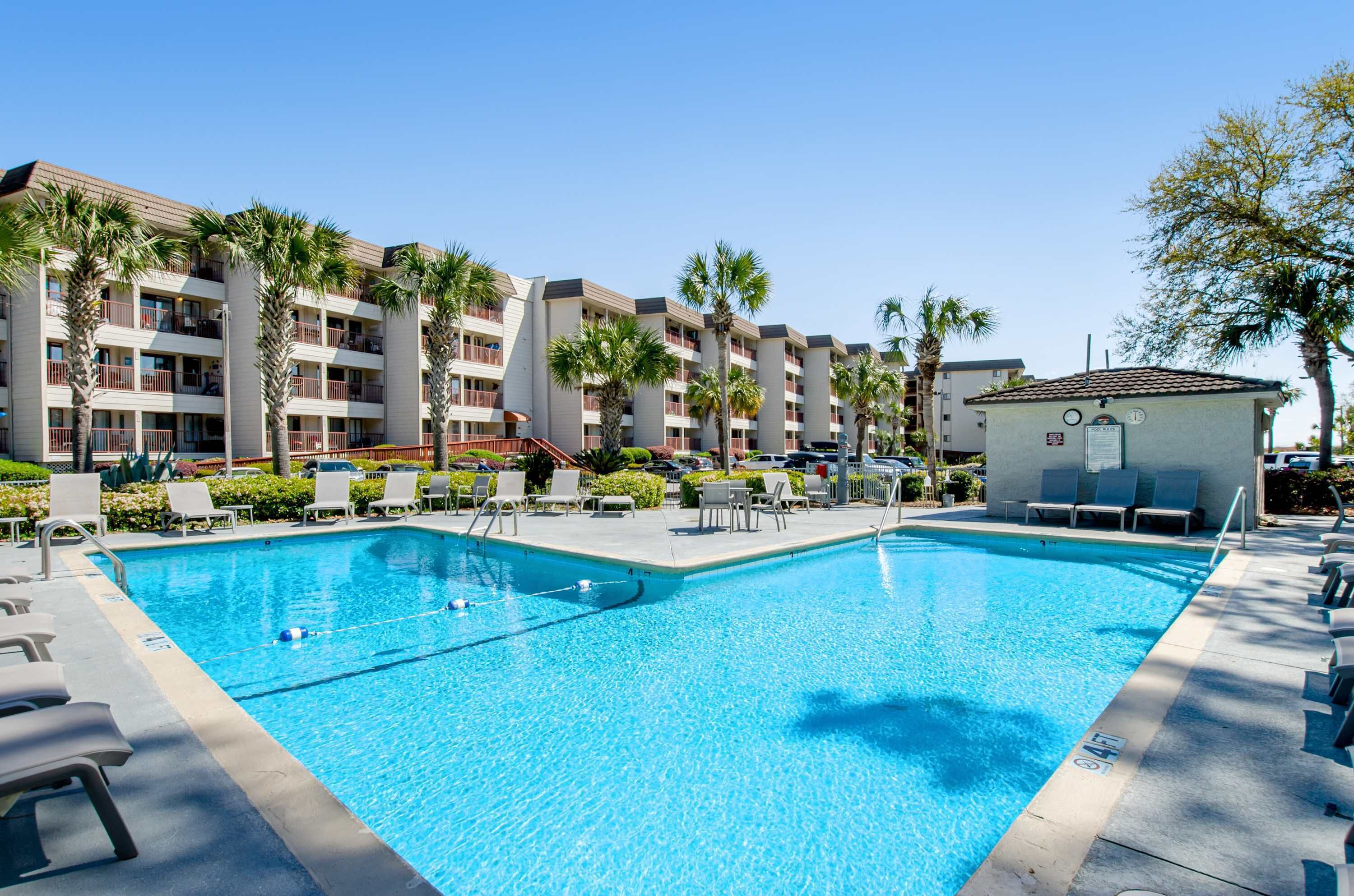 Ein Pool mit Liegestühlen und Palmen, umgeben von einem mehrstöckigen Gebäude.