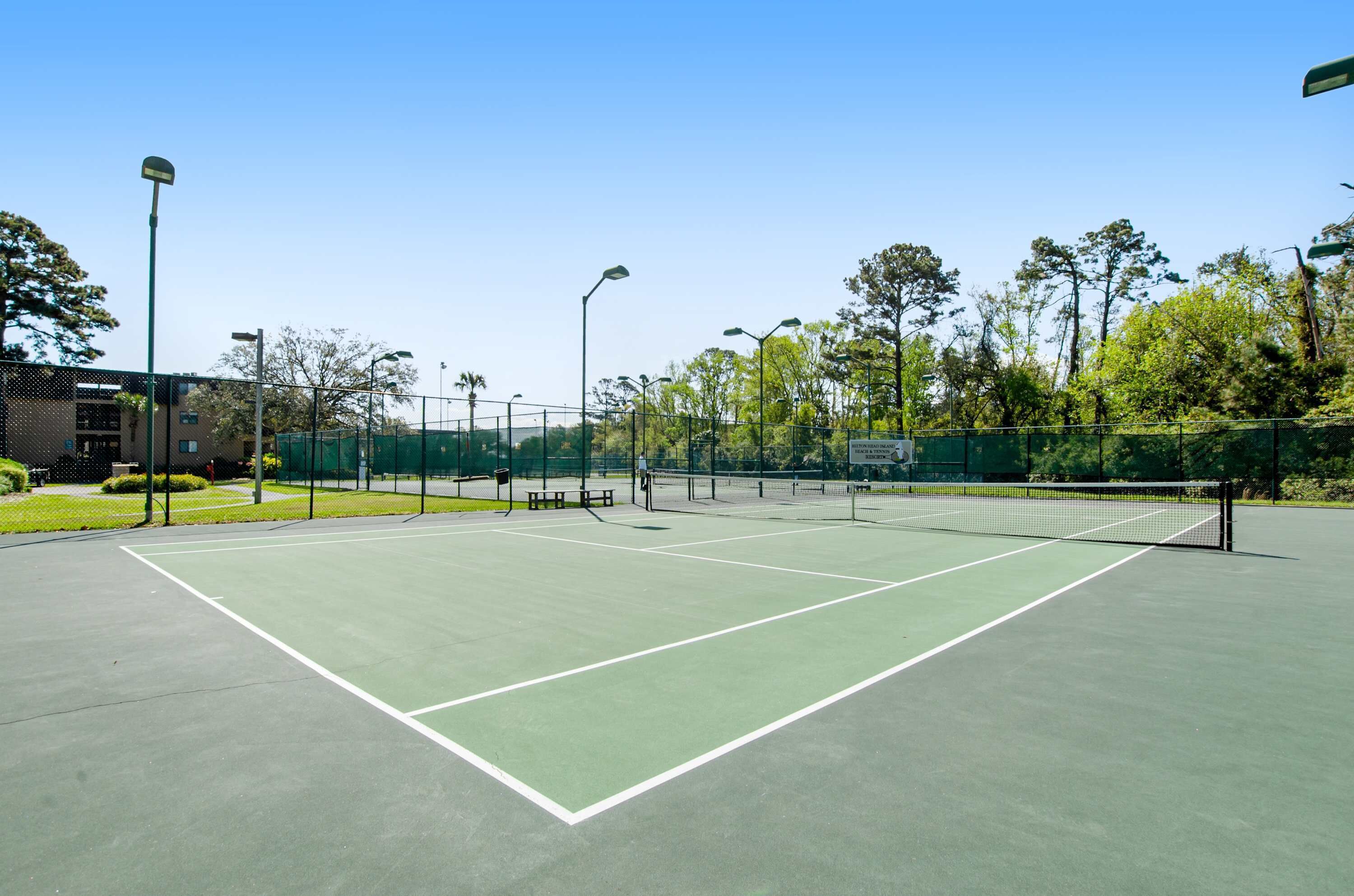 Un court de tennis en plein air, doté d’une surface verte, entouré d’une clôture, avec des arbres en arrière-plan.