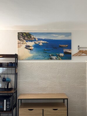 Una pintura de barcos en la playa, una mesa de madera y una zona de cocina con utensilios.