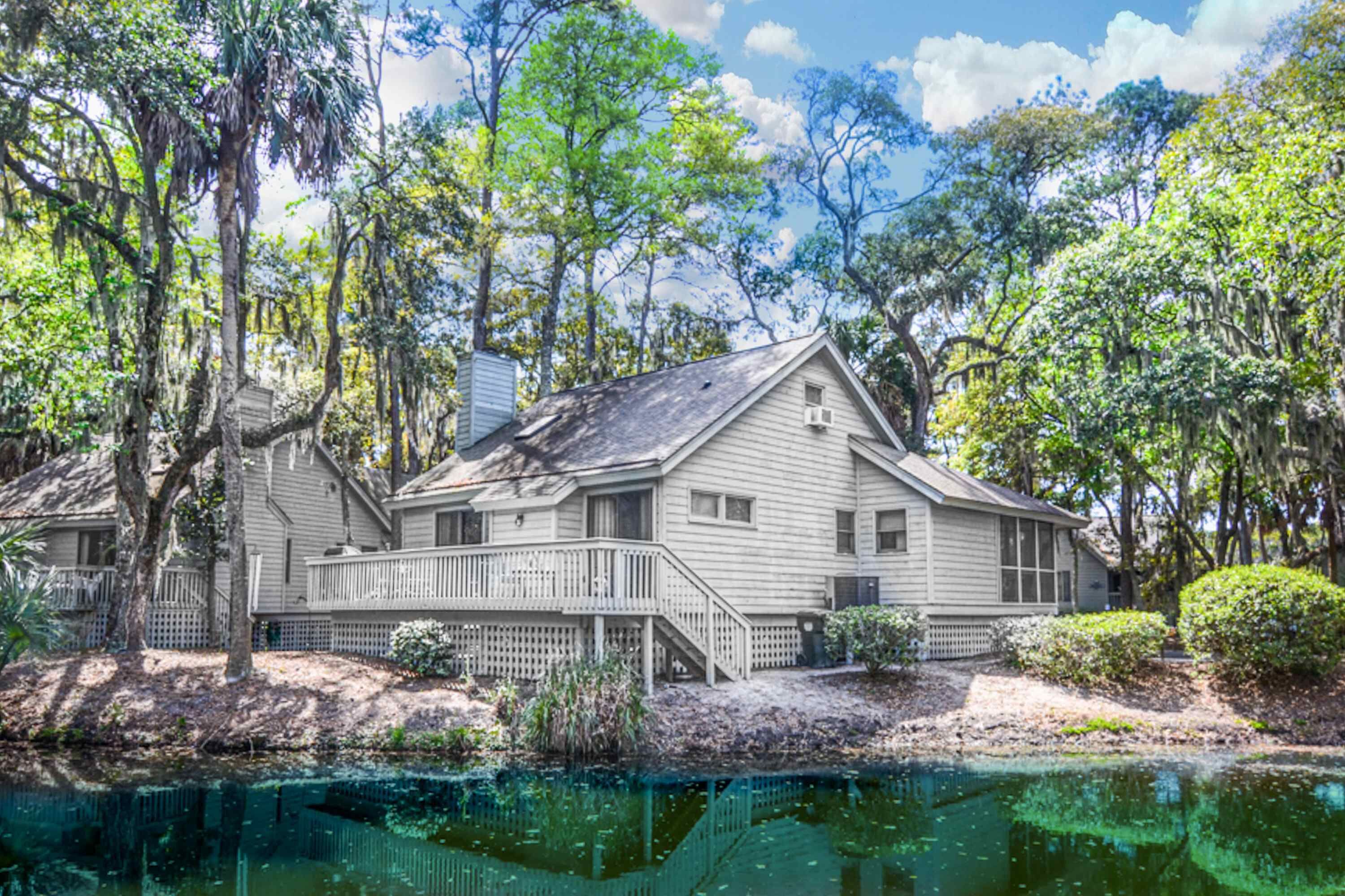 A two-story house with a porch, surrounded by trees and a body of water.