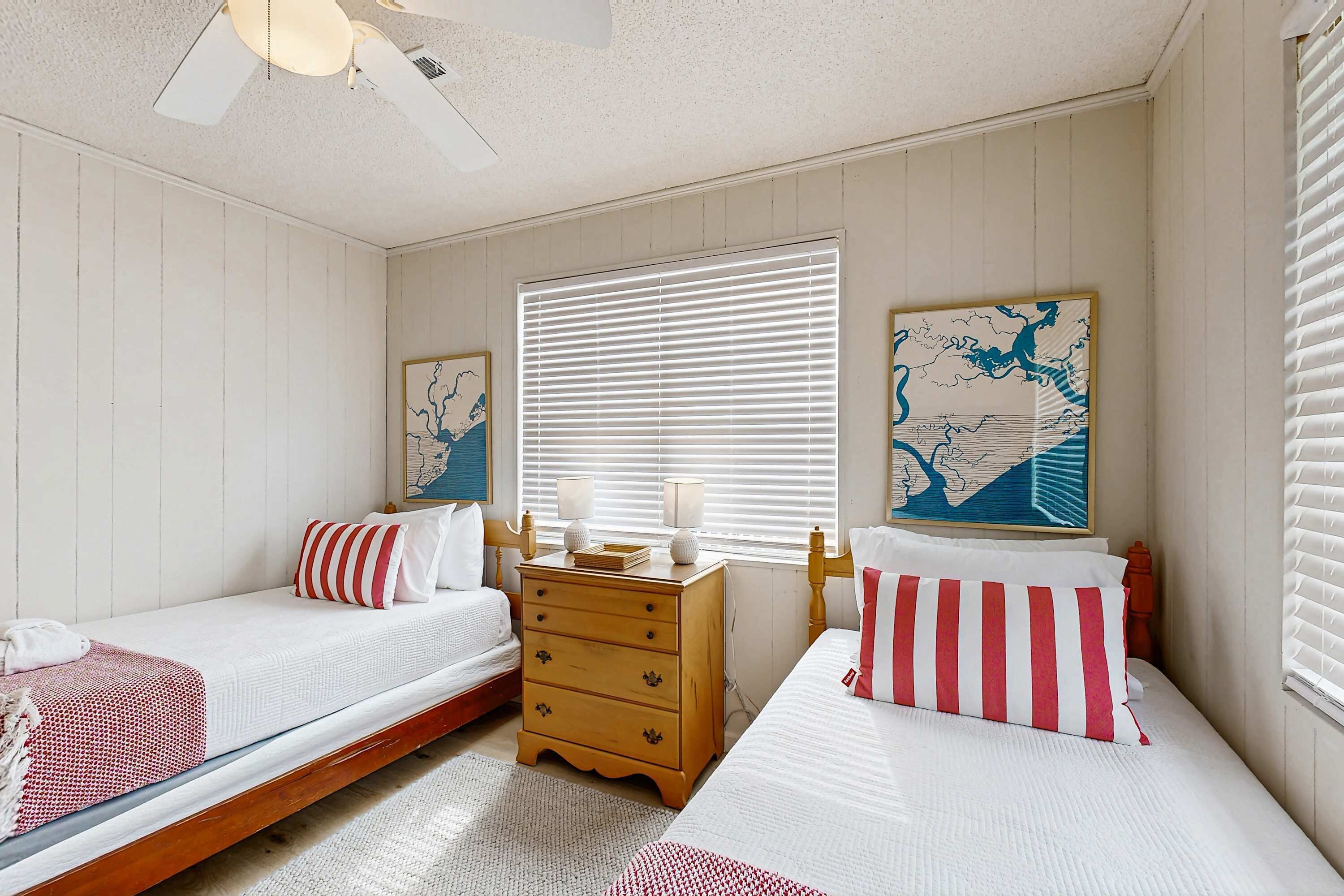 A bedroom with two beds, a wooden dresser, and a ceiling fan.