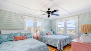 Quarto com duas camas, ventoinha no teto, janelas amplas e vista para o exterior.