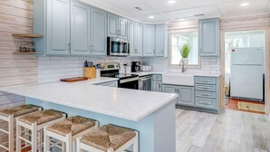 Uma cozinha moderna com armários azul-claros, uma ilha grande com banquetas e uma geladeira.