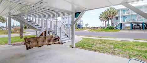 A covered outdoor area with a swing, a bench, and a view of a building with a blue facade.