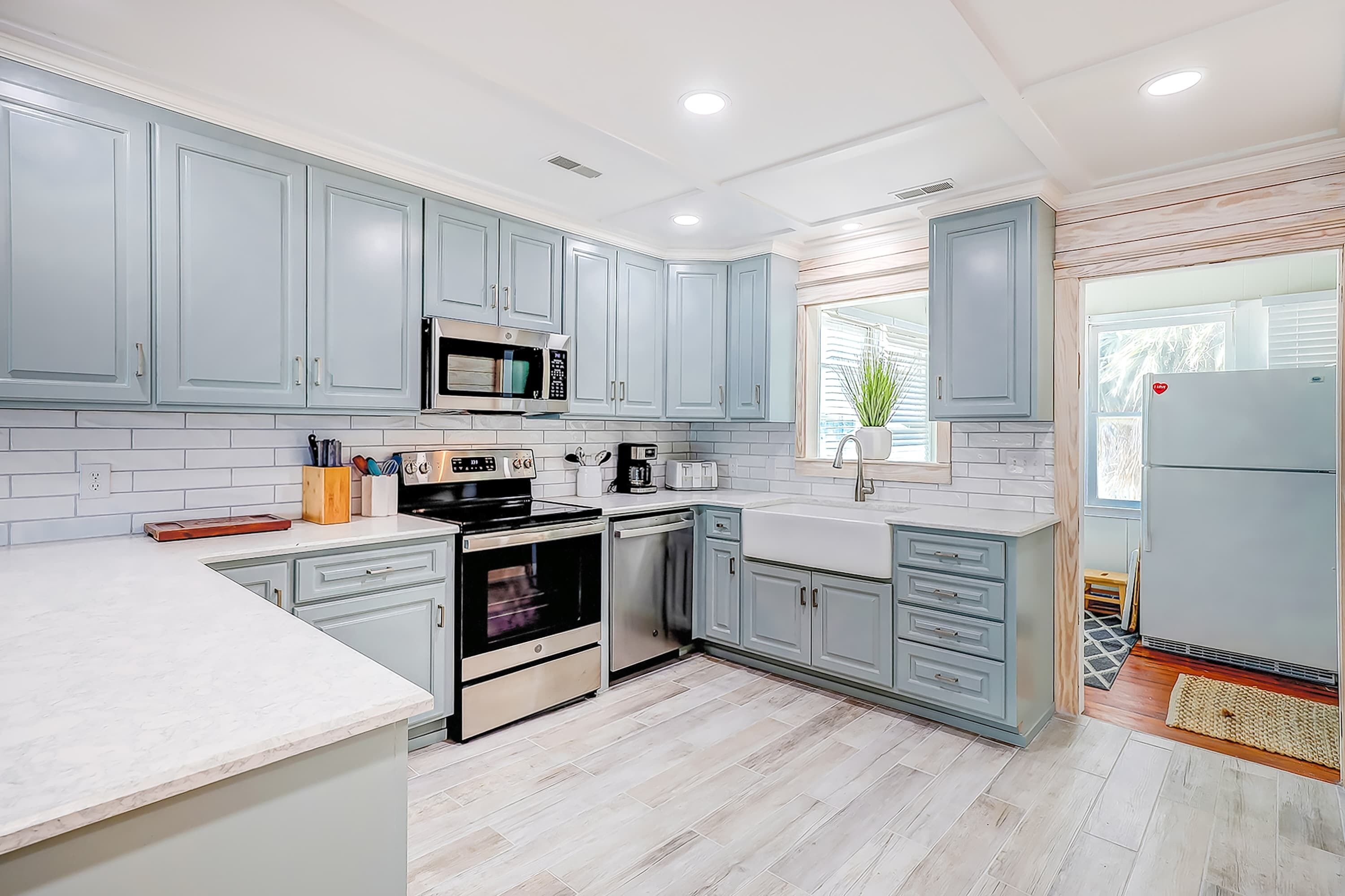 A modern kitchen with light blue cabinets, stainless steel appliances, and a large window.