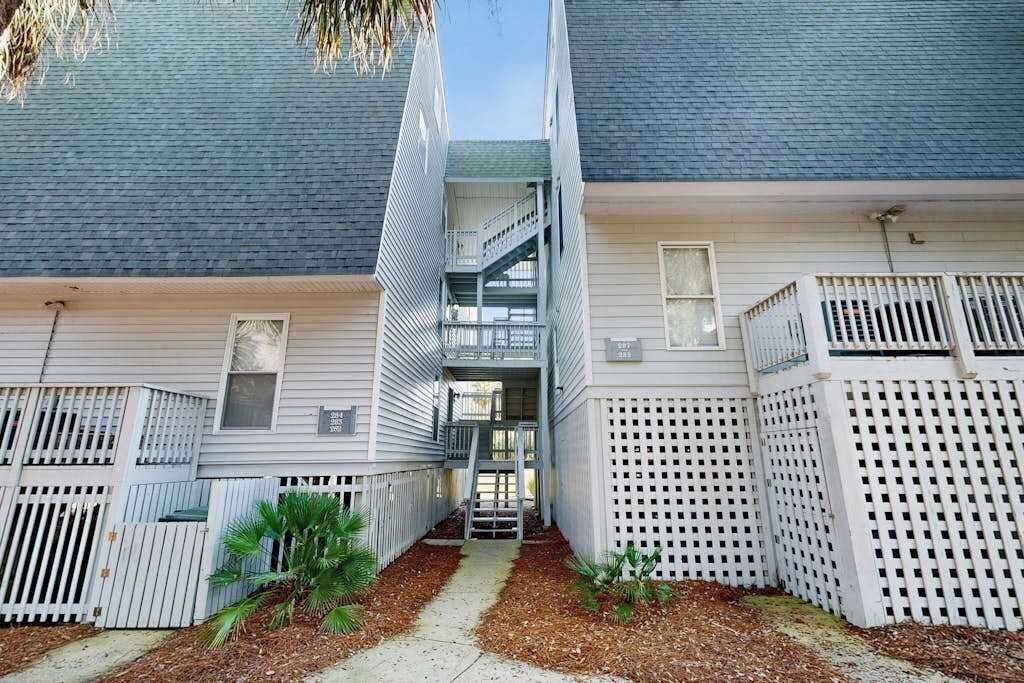 A two-story building with a central staircase, white railings, and a small garden area with plants.