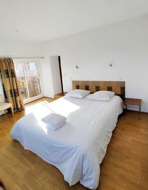 Ein Hotelzimmer mit einem großen Bett, Holzboden, einem Fenster mit Vorhängen und einem Nachttisch.