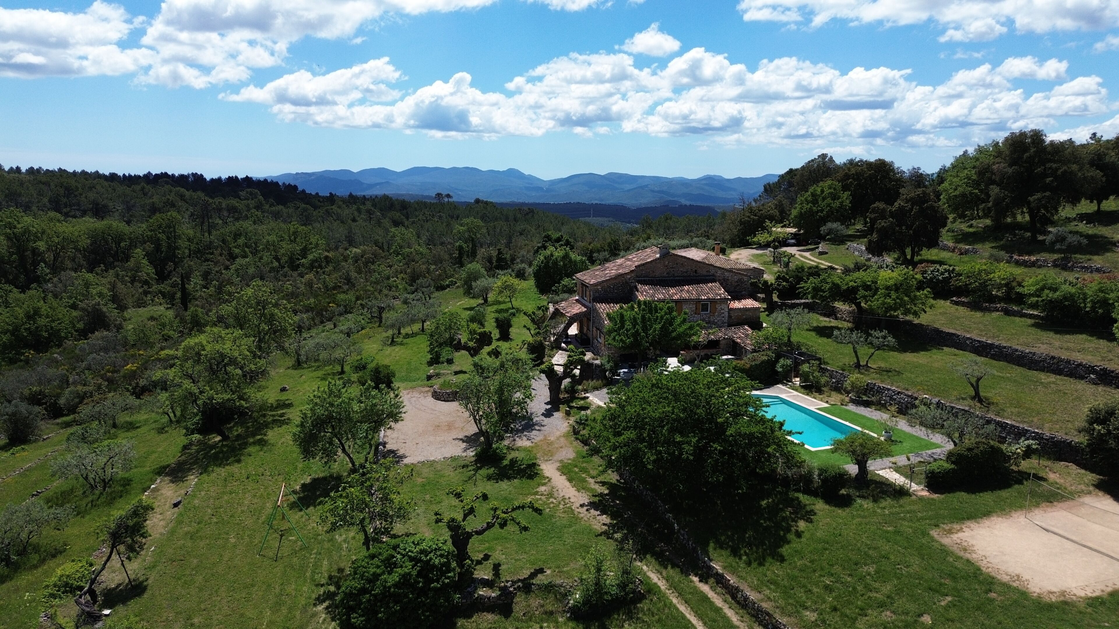 A villa with a swimming pool, surrounded by lush greenery and mountains in the background.