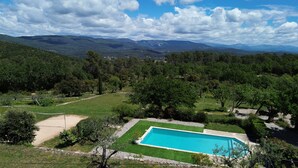 Piscina rodeada por um espaço gramado com árvores e montanhas ao fundo.