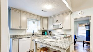 A kitchen with white cabinets, a granite countertop, a microwave, and a sink. - Spacious Tropical Home w/ Patio, Free WiFi & Screened-In Porch (Edisto Beach)