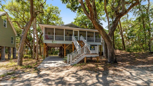 A two-story wooden house with a balcony, surrounded by trees. - Spacious Tropical Home w/ Patio, Free WiFi & Screened-In Porch (Edisto Beach)