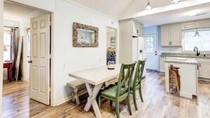 A kitchen with white cabinets, a dining table with chairs, and a small island with a stool. - Spacious Tropical Home w/ Patio, Free WiFi & Screened-In Porch (Edisto Beach)