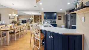Une cuisine moderne avec des meubles de couleur sombre, un îlot central et un coin repas comprenant des chaises et une table en bois.
