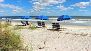 Een strand met blauwe parasols, ligbedden en een zandstrand.