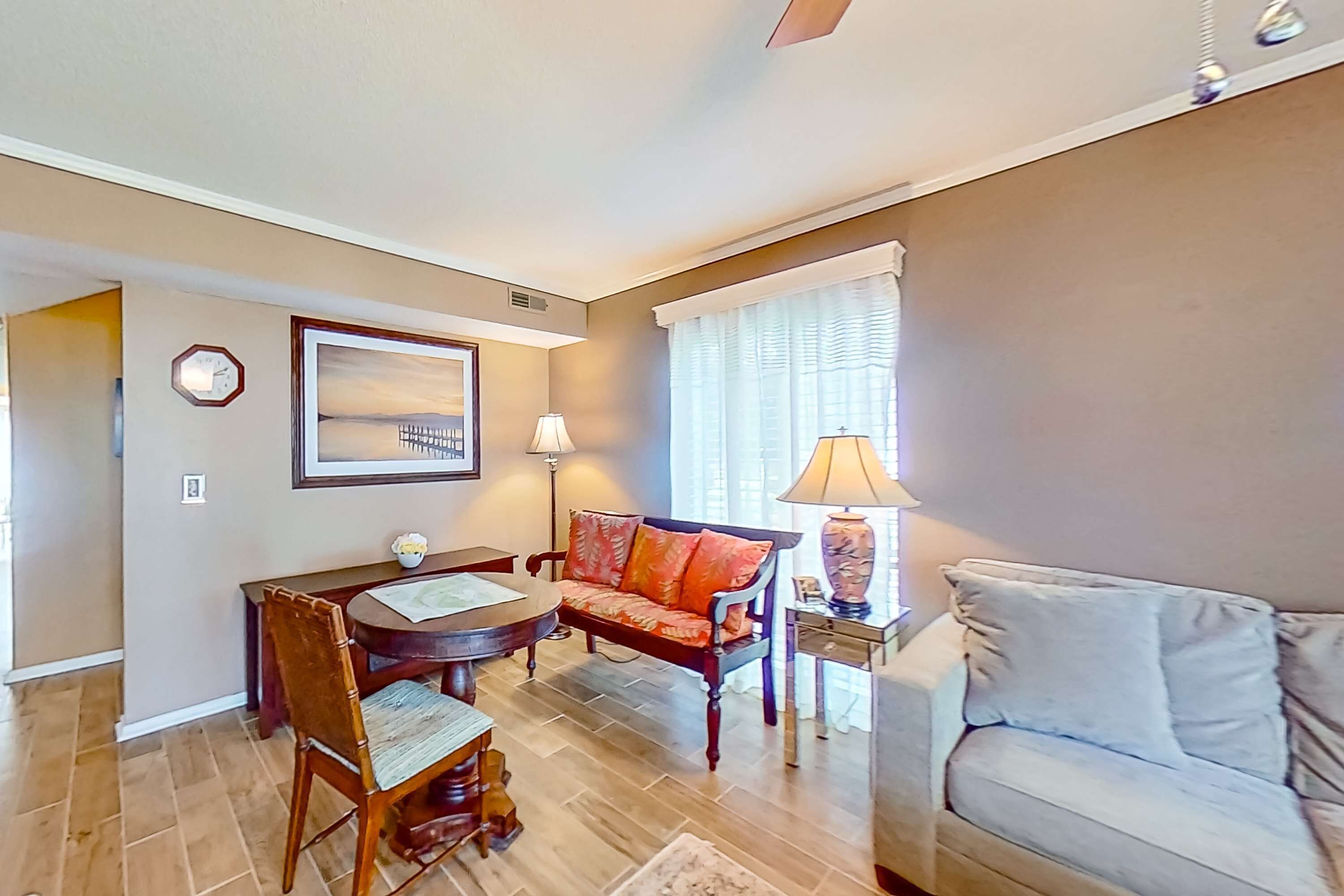 A living room with a sofa, a dining table with chairs, a lamp, and a clock on the wall.