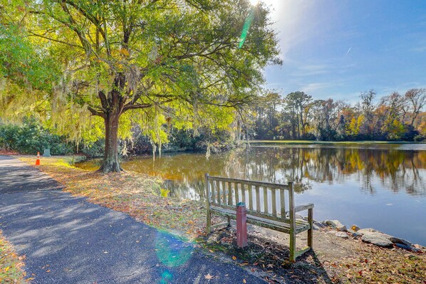 Un parc amb una banca al costat d'un llac, arbres i un cel serè.
