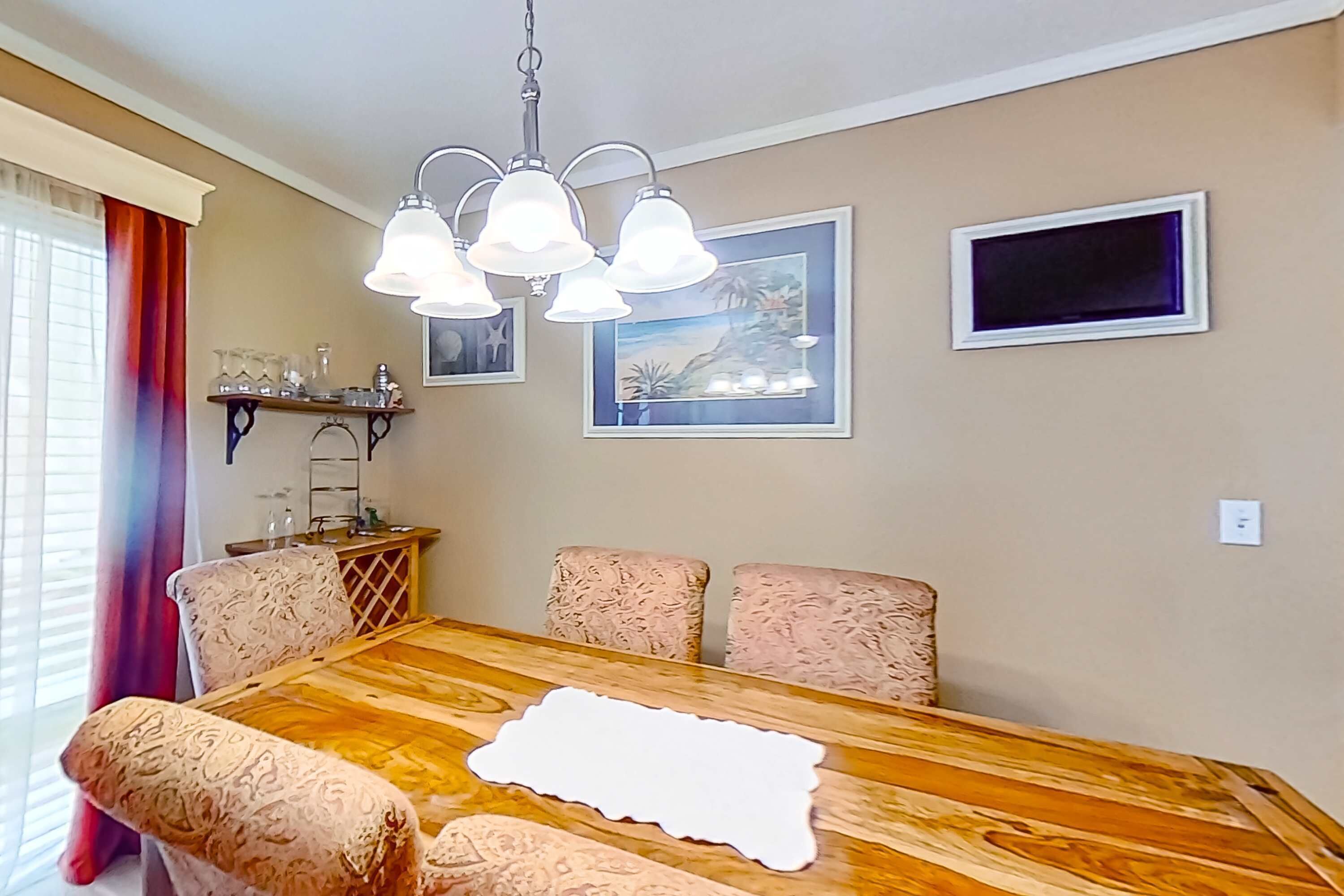 A dining area with a wooden table, patterned chairs, a chandelier, and framed artwork on the wall.