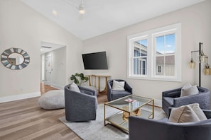 Een moderne woonkamer met een flatscreen televisie, comfortabele zithoek en een groot raam.
