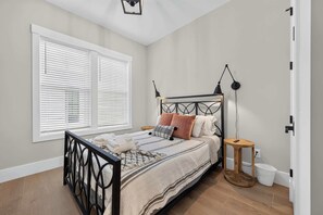 Quarto com cama, abajures, mesa de cabeceira, janela com persianas e porta.