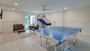 A ping pong table in a room with a ceiling fan, a bench, and a small seating area.
