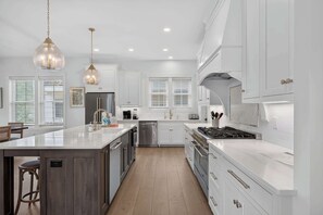 A modern kitchen with white cabinetry, a large island, stainless steel appliances, and pendant lighting. - North Forest Beach home with a private pool and four primary suites (Hilton Head)