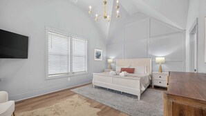 A bedroom with a large bed, bedside tables, a flat-screen TV, and a chandelier.