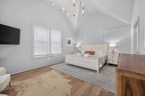 A bedroom with a large bed, bedside tables, a flat-screen TV, and a chandelier. - North Forest Beach home with a private pool and four primary suites (Hilton Head)