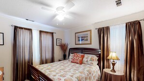 A bedroom with a bed, a bedside table with a lamp, a ceiling fan, and curtains. - A Block and a Half to the Beach Dog-Friendly Home w/ Screened Porch & WiFi (Edisto Beach)