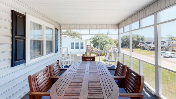 A covered patio with a table and chairs, large windows, and a view of a residential area. - A Block and a Half to the Beach Dog-Friendly Home w/ Screened Porch & WiFi (Edisto Beach)