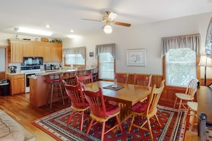 A spacious kitchen with wooden cabinets, a dining area with a large table and red chairs, and a ceiling fan.