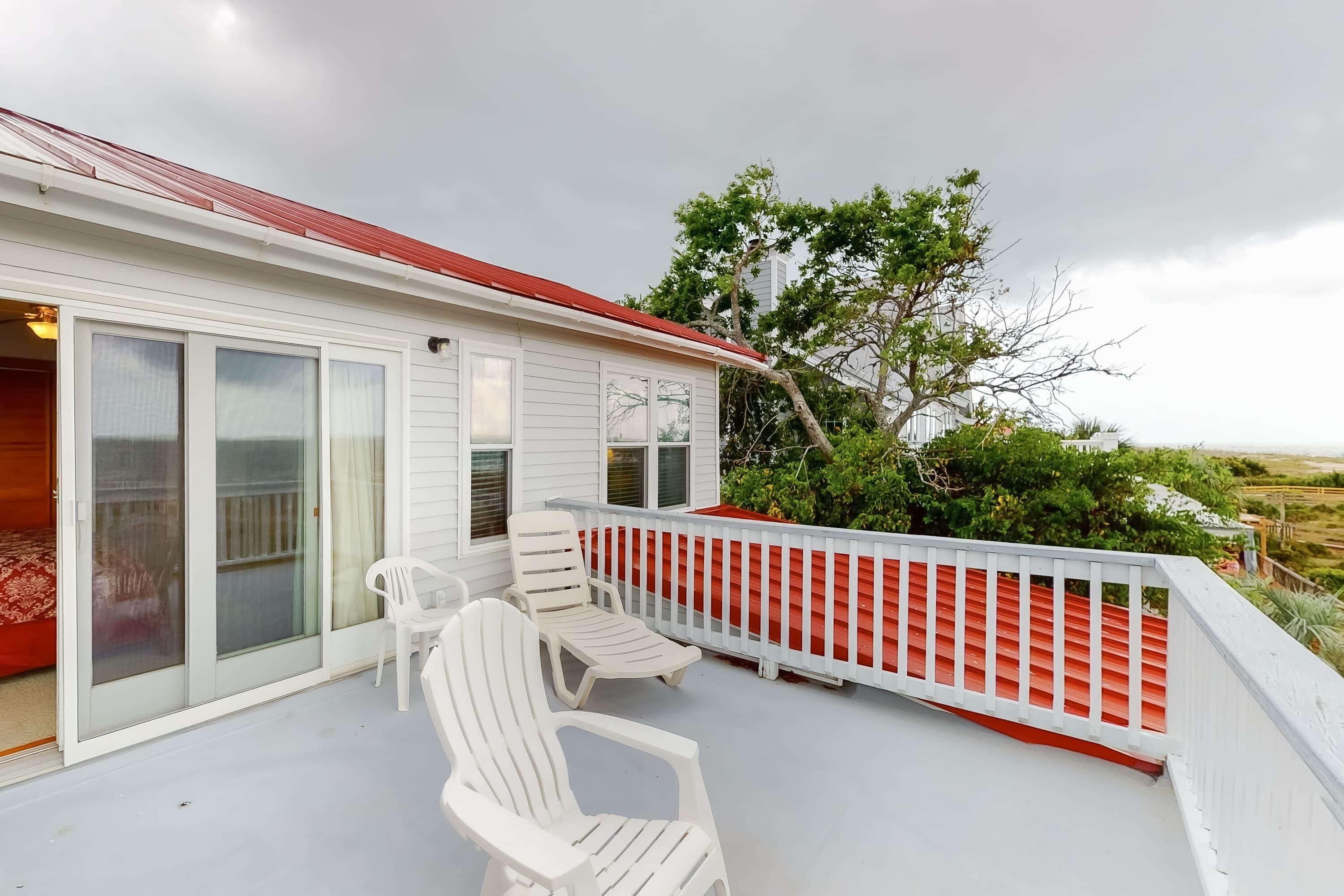Une maison à l’extérieur blanc, avec un toit rouge et une véranda couverte dotée de chaises blanches.