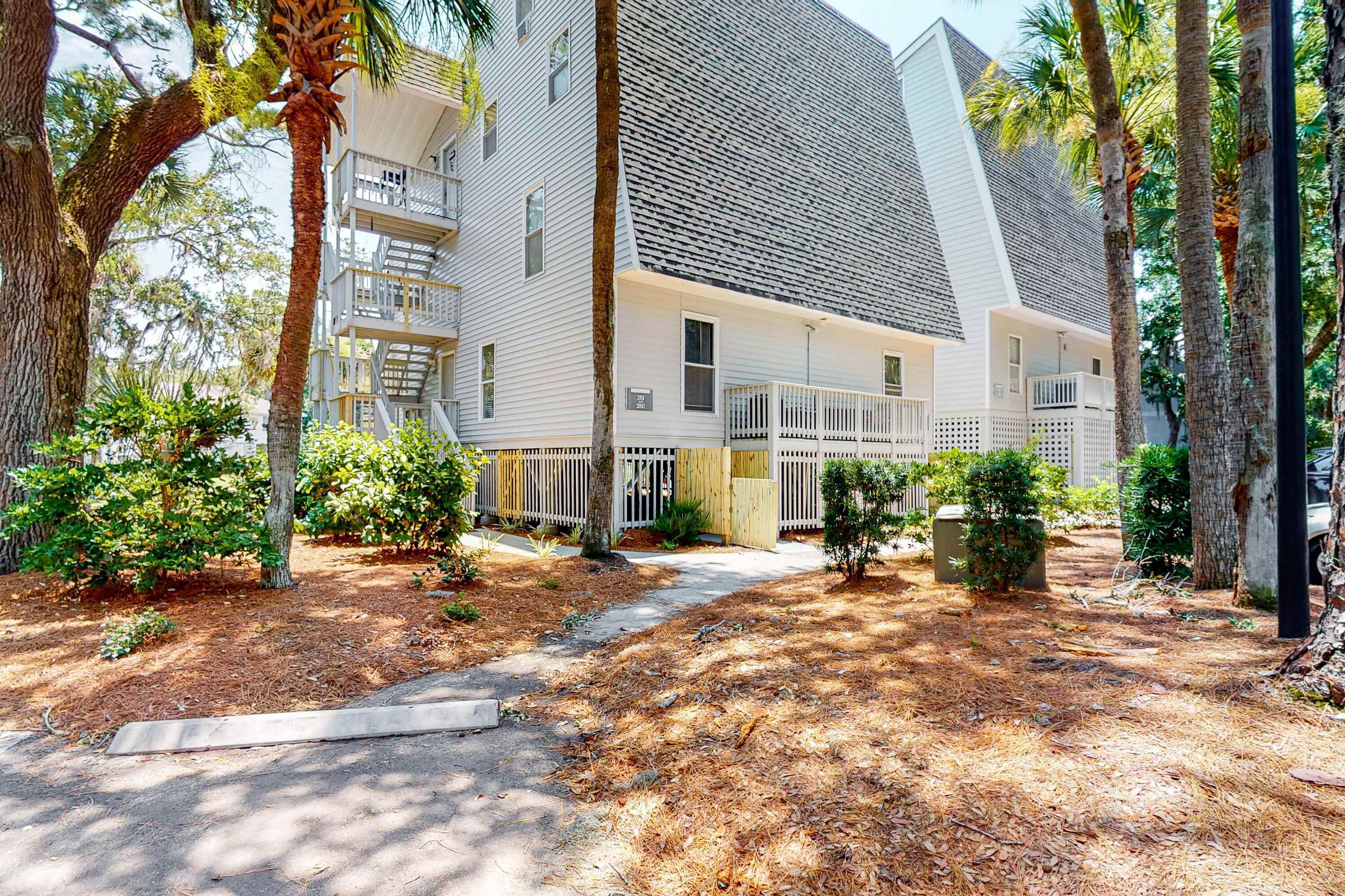 A multi-story residential building with a covered porch, trees, and a pathway.