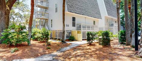 A multi-story residential building with a covered porch, trees, and a pathway.