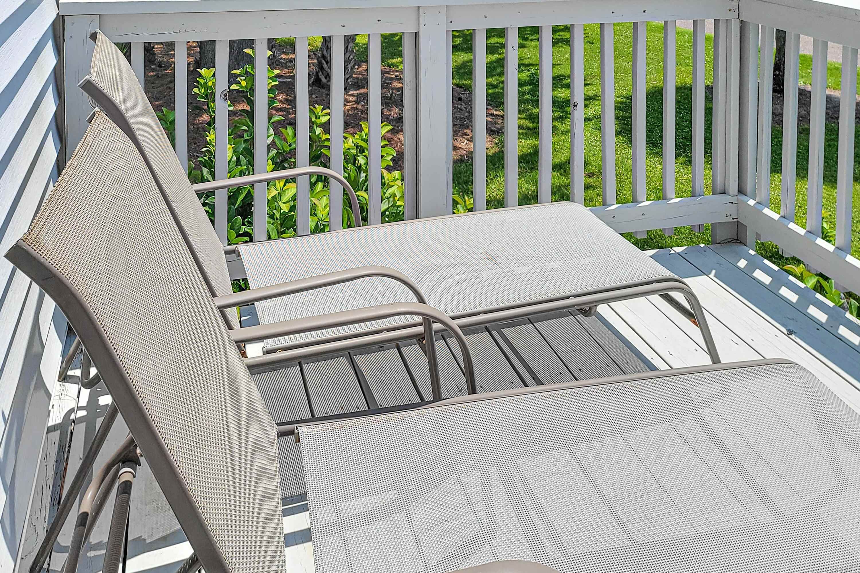 Un área de estar exterior de metal con barandilla blanca, una mesa metálica y una silla metálica.