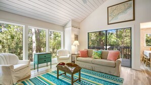 A spacious living room with large windows, a wooden ceiling, a sofa, a chair, a coffee table, and a map on the wall. - Walk to Beach 2BR with loft Condo on Beautiful Edisto Beach, SC (Edisto Beach)