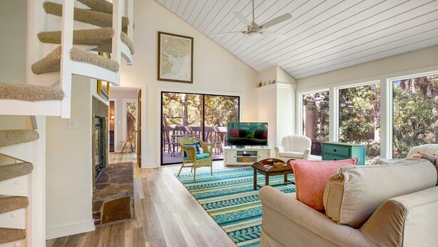 A spacious living area with a staircase, a television, a sofa, and a view of the outdoors. - Walk to Beach 2BR with loft Condo on Beautiful Edisto Beach, SC (Edisto Beach)
