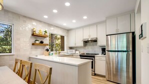 A modern kitchen with a central island, white cabinetry, stainless steel appliances, and wooden chairs. - Walk to Beach 2BR with loft Condo on Beautiful Edisto Beach, SC (Edisto Beach)