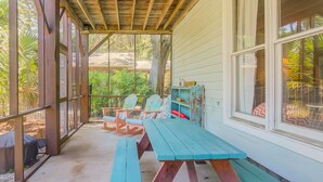 Een overdekte veranda met houten banken en stoelen, een tafel en een raam met uitzicht op groen.