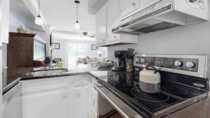 Una cucina con mobili bianchi, un piano cottura nero e una ventola a soffitto.