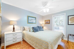 A bedroom with a bed, nightstand, lamp, ceiling fan, and framed pictures on the wall.